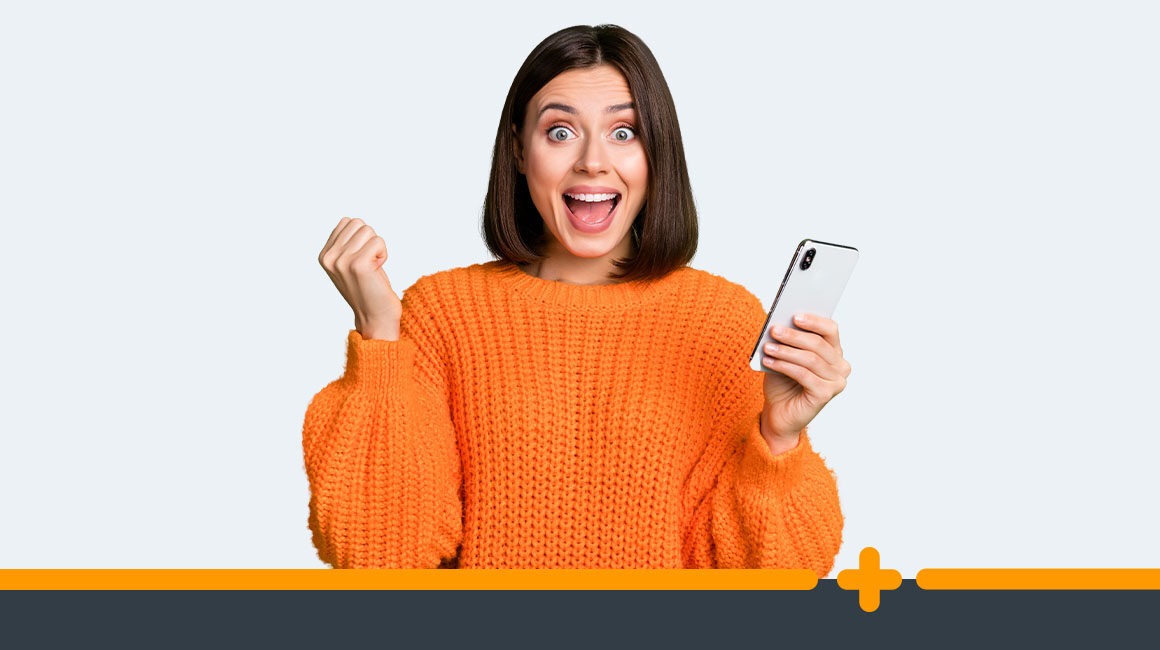 Zachwycona młoda kobieta w pomarańczowym swetrze trzymająca smartfon