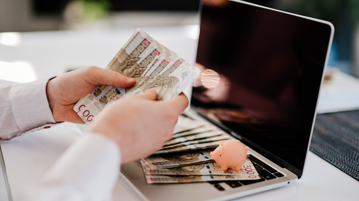 Mężczyzna liczący polskie banknoty przy laptopie

